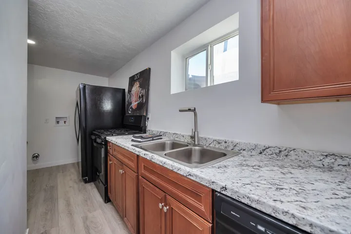 Kitchen featuring wood cabinetry, a double basin stainless steel sink with a modern faucet, and light-toned, patterned countertops