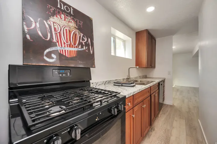Kitchen featuring a black gas range, white speckled countertops, wood-finish cabinetry, a stainless steel sink, and light wood-finish flooring