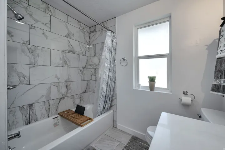 Full bath featuring a tub-shower combination with floor-to-ceiling tile surround and a window with frosted glass