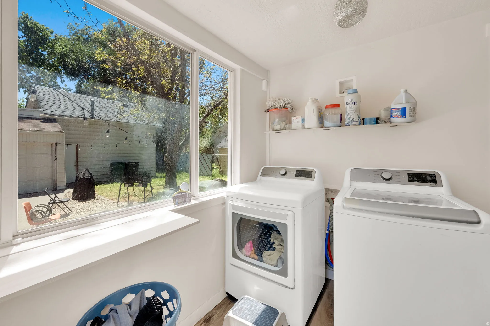Bright laundry area featuring a large window, white walls, and wood-finish flooring