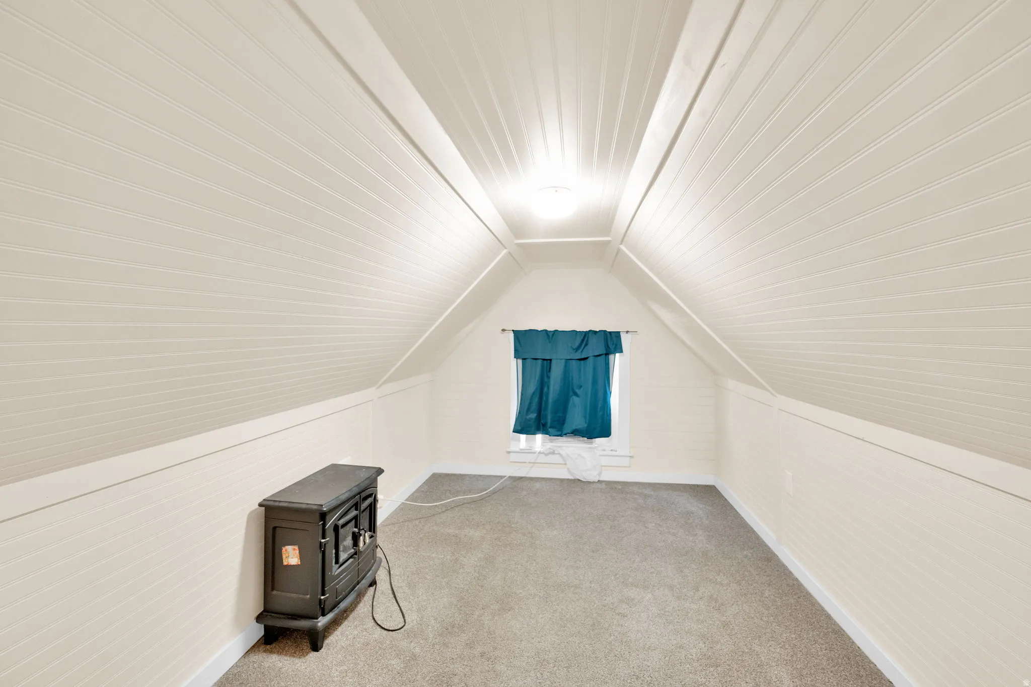 Attic space featuring vaulted ceilings with beadboard paneling, neutral carpeting, and a single window