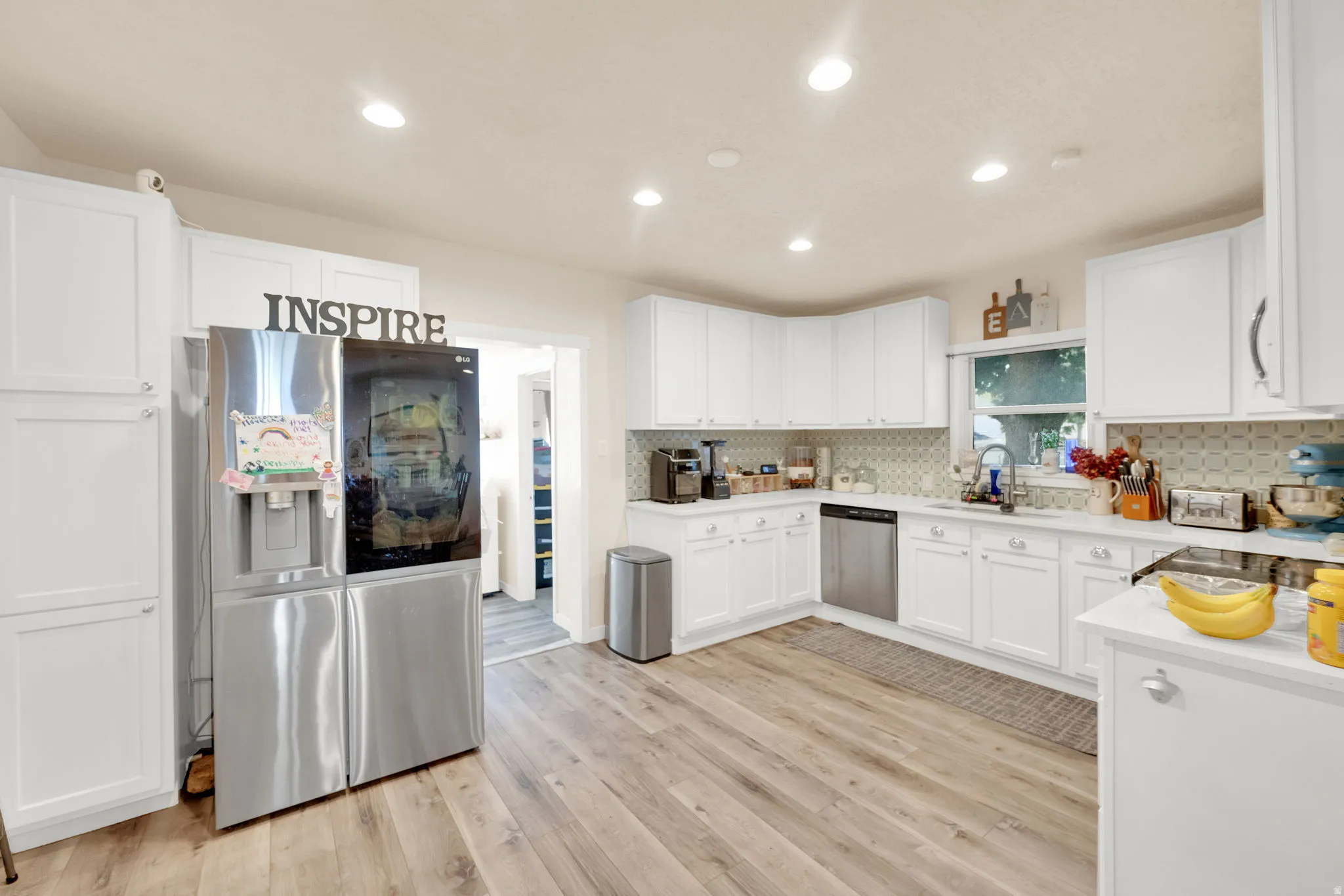 Bright kitchen featuring white cabinetry, wood-finish flooring, recessed lighting, and a patterned tile backsplash