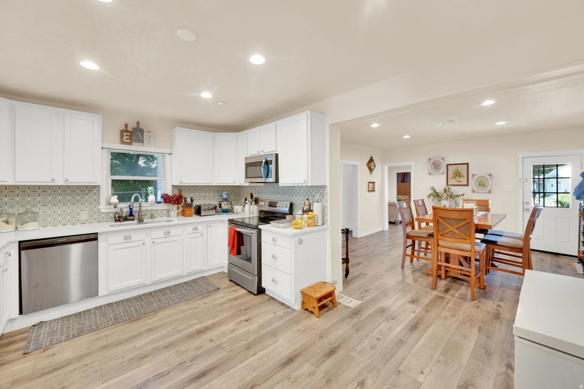 Bright kitchen featuring white cabinetry, stainless steel appliances, wood-finish flooring, recessed lighting, and an open concept dining area