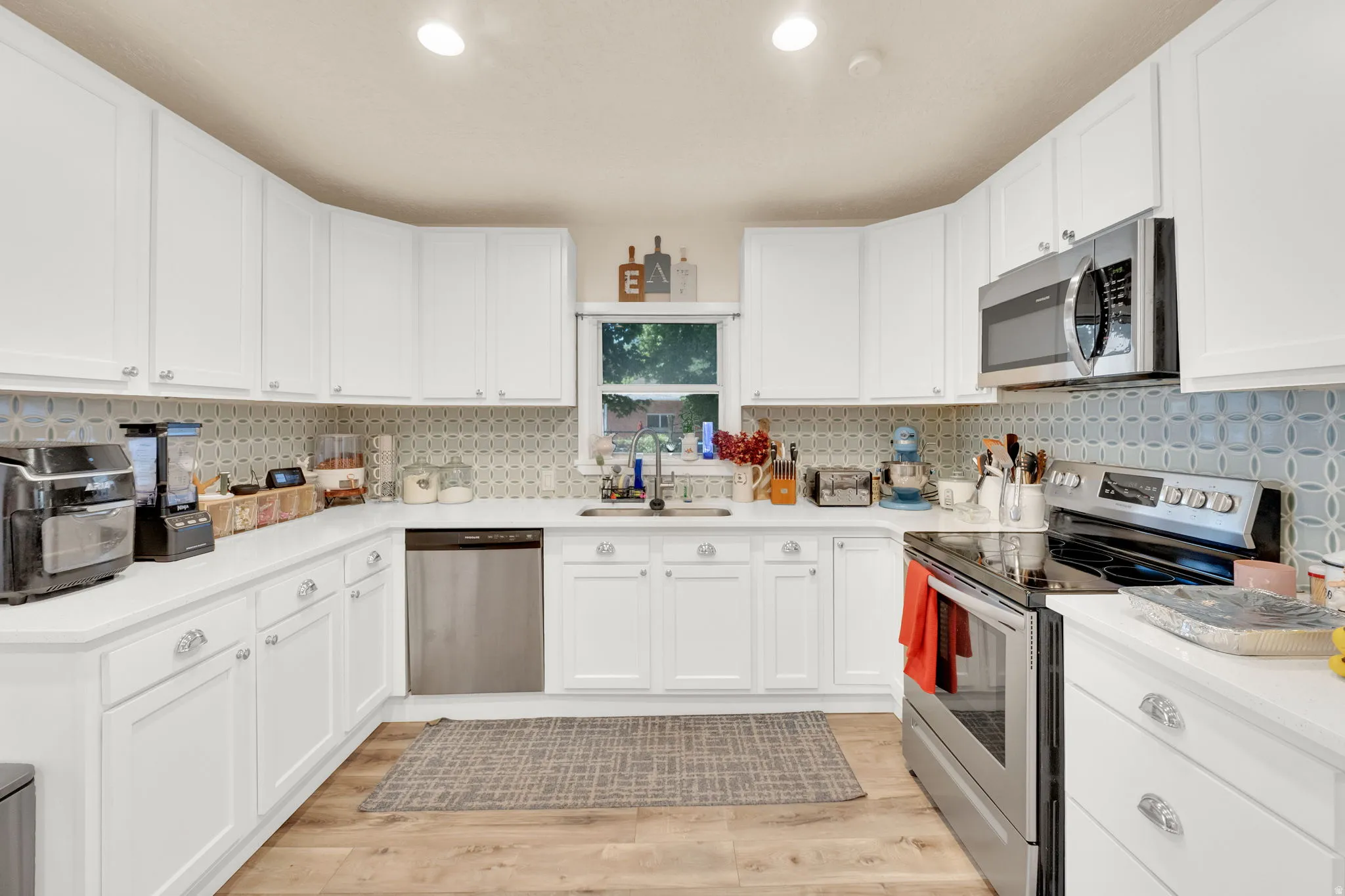 Kitchen featuring extensive white cabinetry, light countertops, wood-finish flooring, stainless steel appliances, and a tiled backsplash
