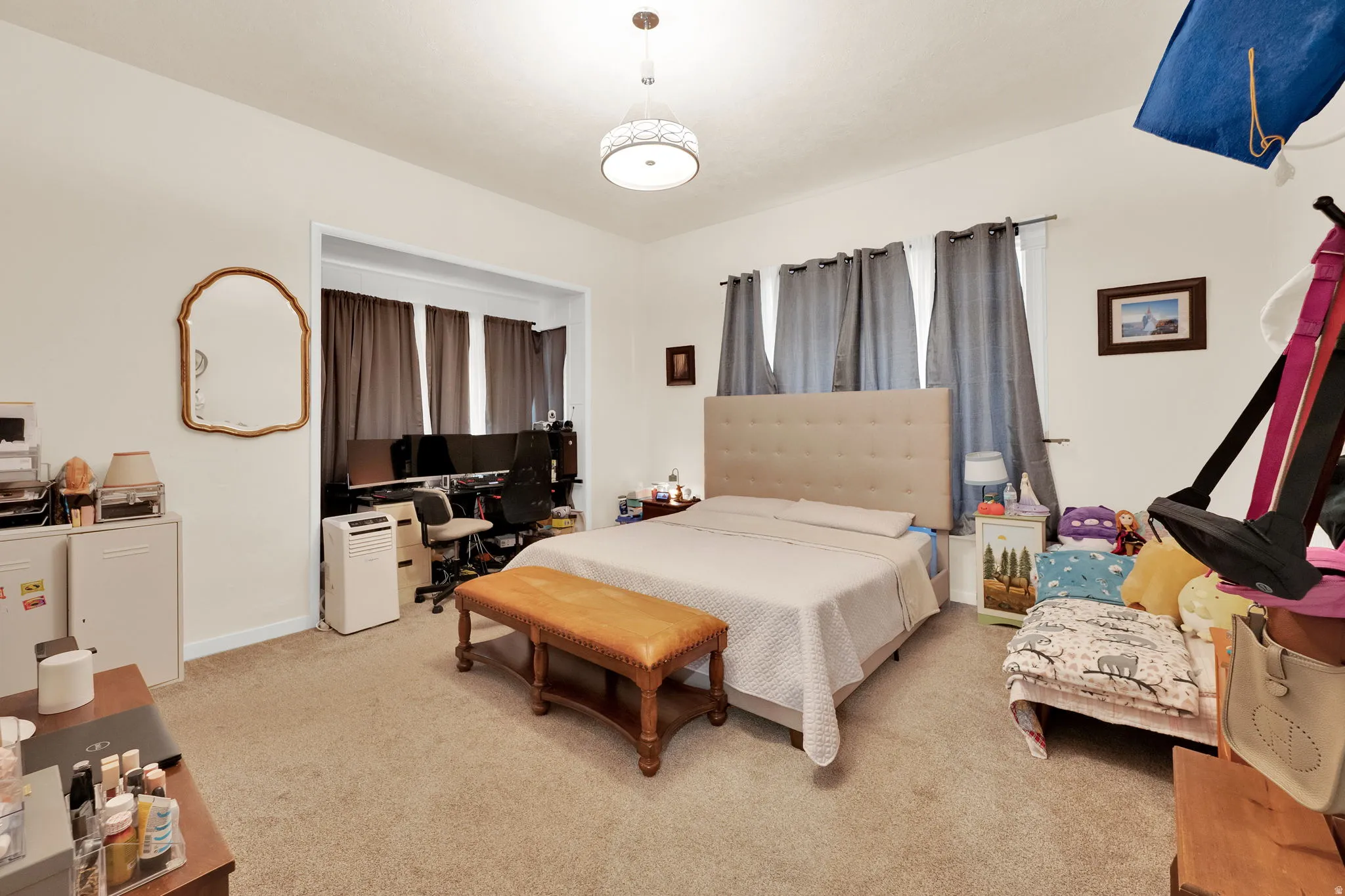 Expansive carpeted room featuring a neutral color palette, recessed area with three windows, and a flush-mount ceiling light fixture
