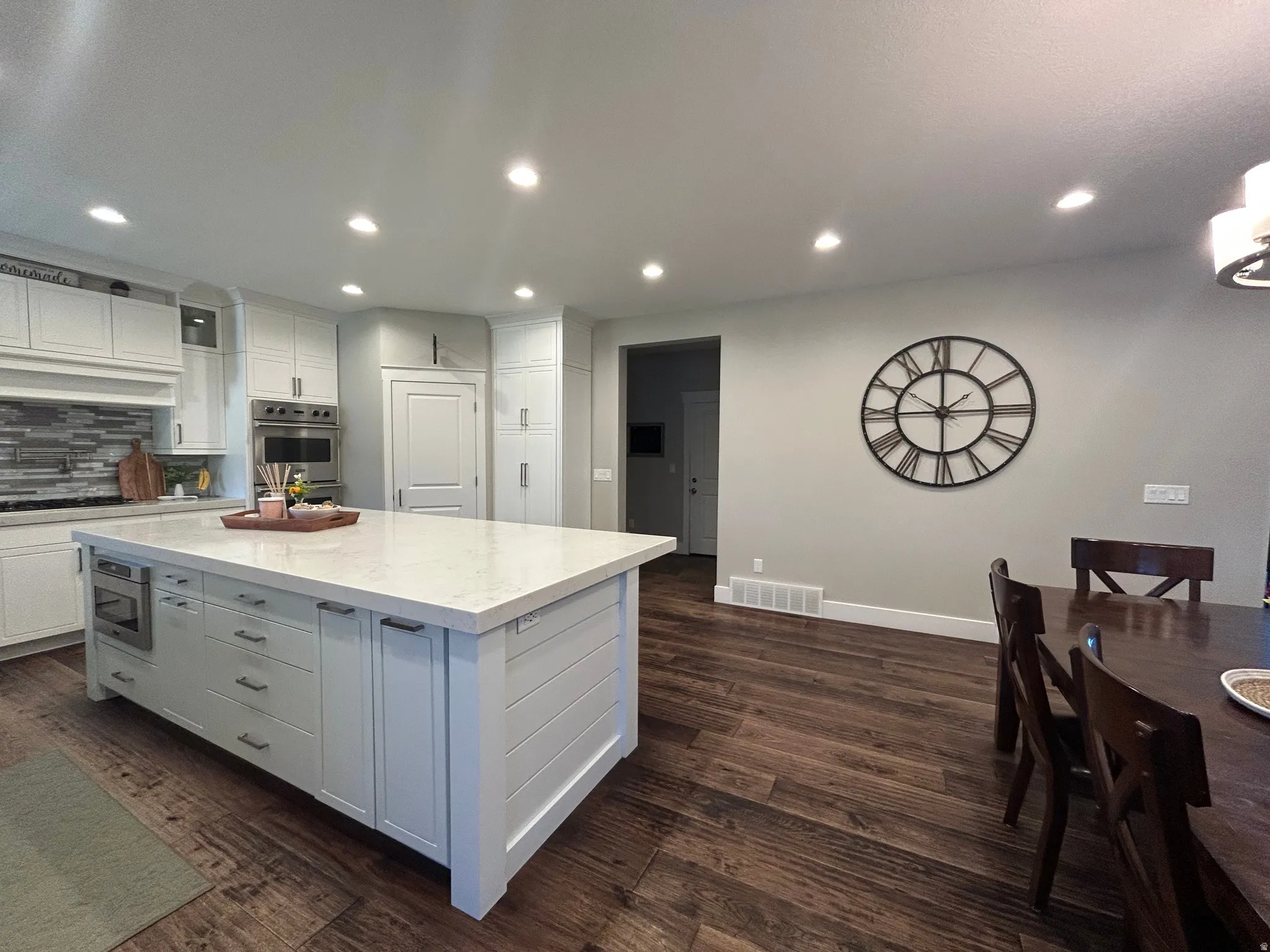 Gourmet kitchen featuring a large island with a light-toned countertop, stainless steel appliances, extensive white cabinetry, and wood-finish flooring