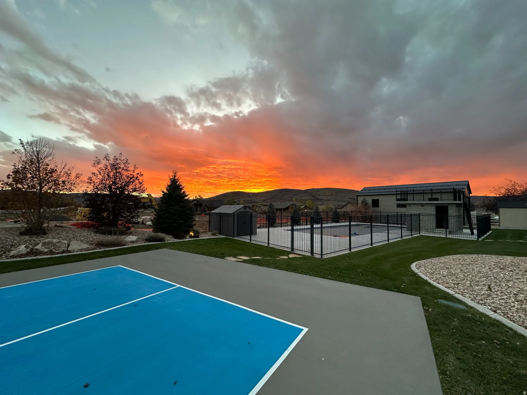Recreational court with blue and gray surfacing, manicured lawn, and a fenced swimming pool