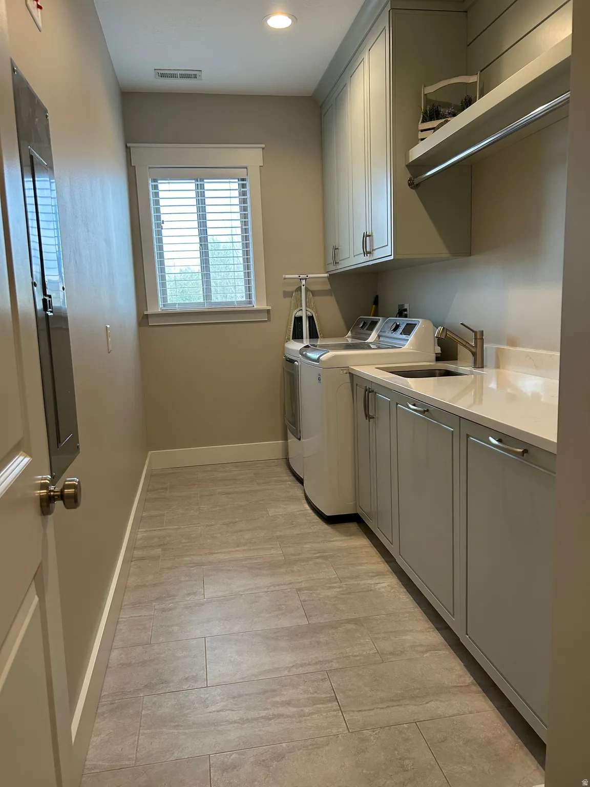 Laundry room featuring light gray cabinetry, a built-in sink with a gooseneck faucet, light countertops, and plank-style floor tiling