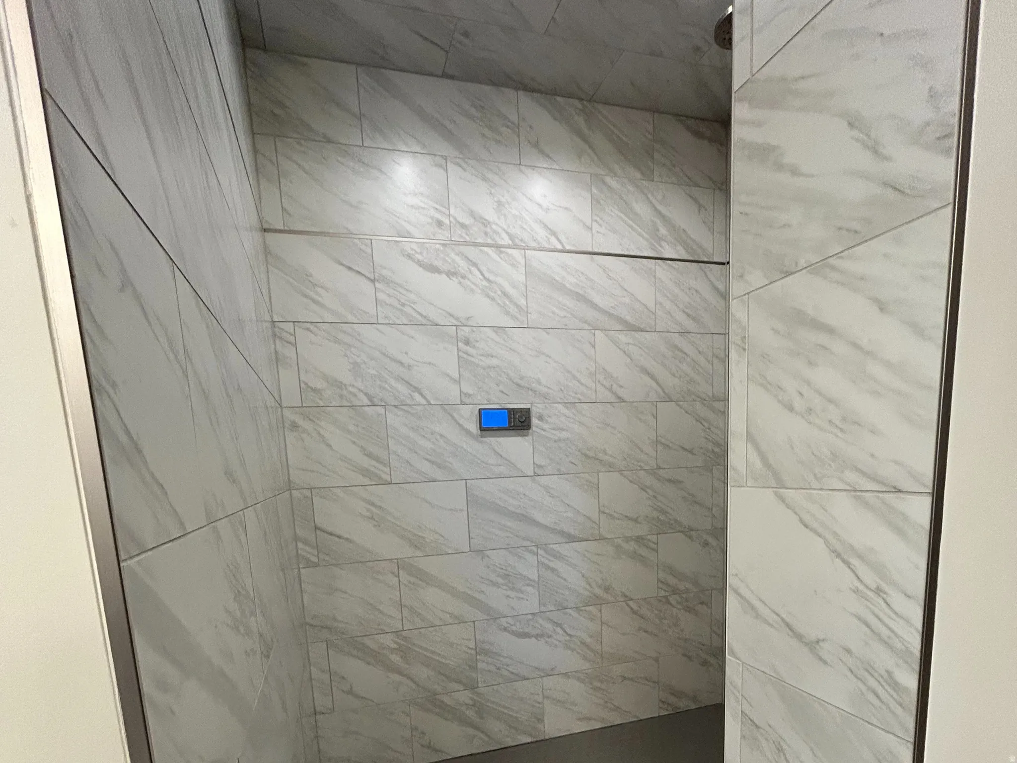 Walk-in shower featuring light-toned large format wall tiling, a dark hexagonal tile floor, recessed lighting, and a digital shower control panel