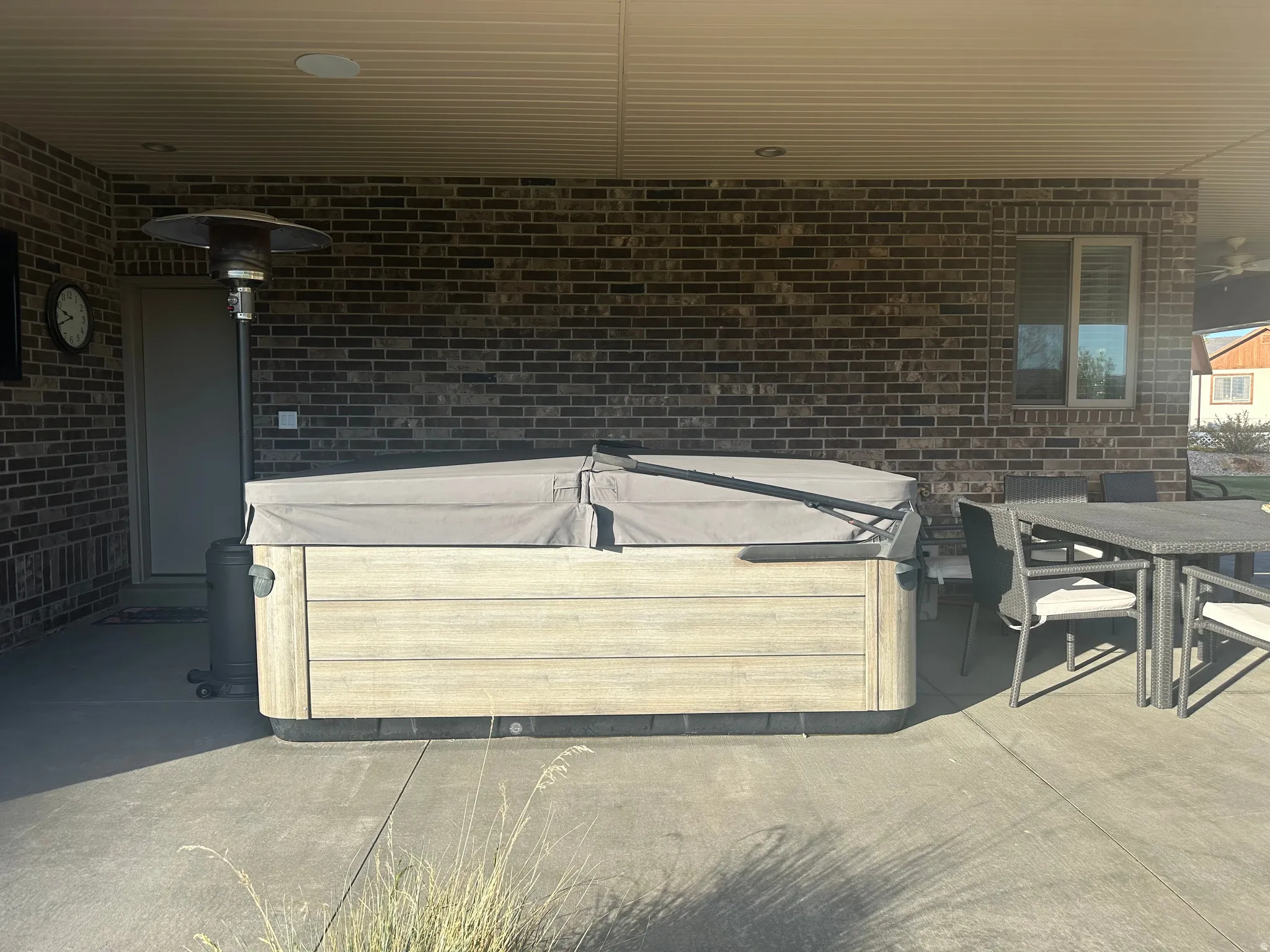Covered patio featuring a hot tub with a light wood-finish exterior, concrete flooring, and a brick exterior wall
