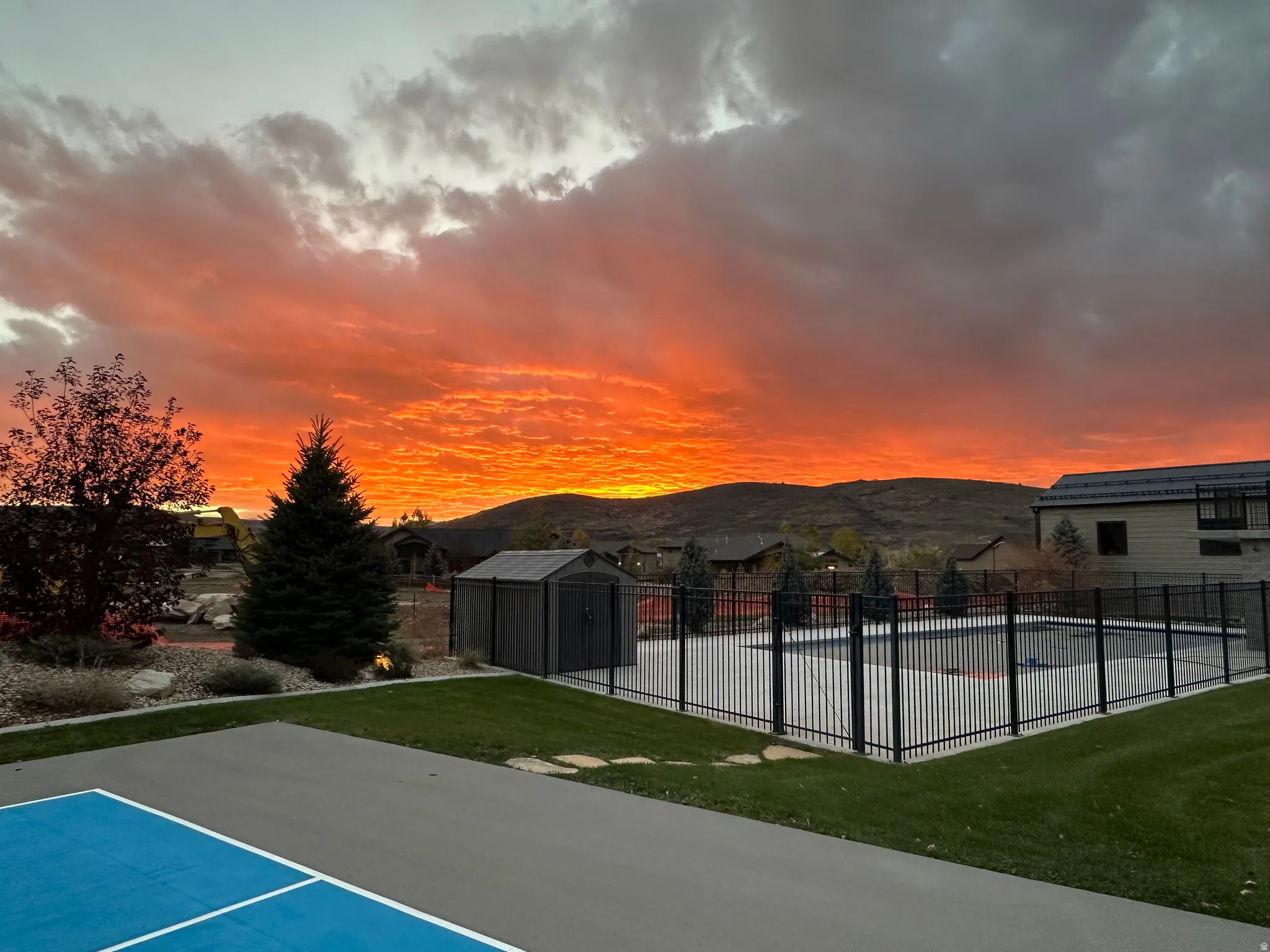 Outdoor recreational amenities featuring a fenced swimming pool, adjacent storage shed, and a hard surface court with blue playing lines