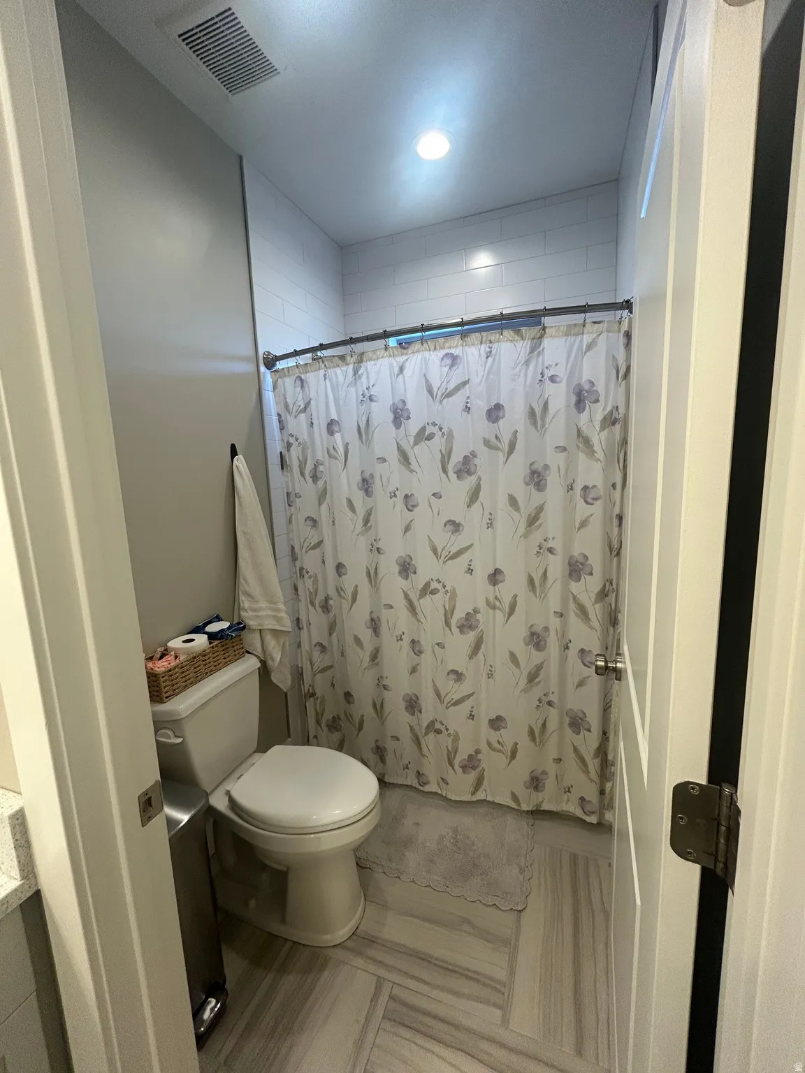 Bathroom featuring a walk-in shower with white subway tile, a white toilet, and wood-finish flooring in a herringbone pattern