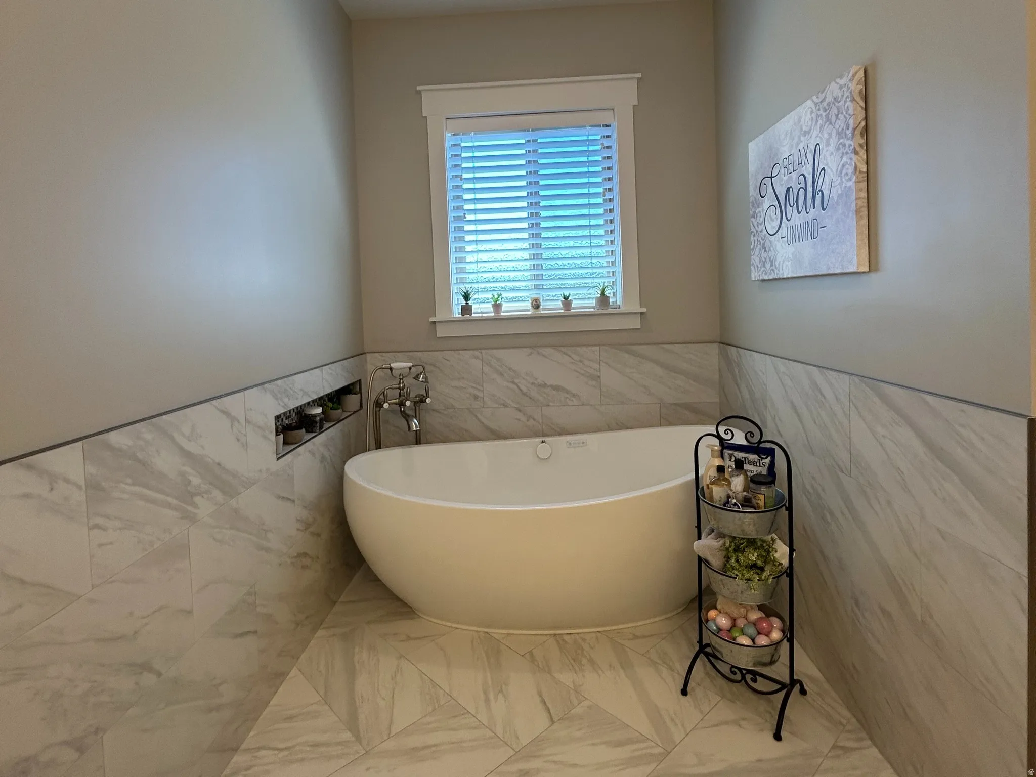 Freestanding soaking tub with floor-mounted faucet, complemented by wall-to-ceiling tile in a neutral tone