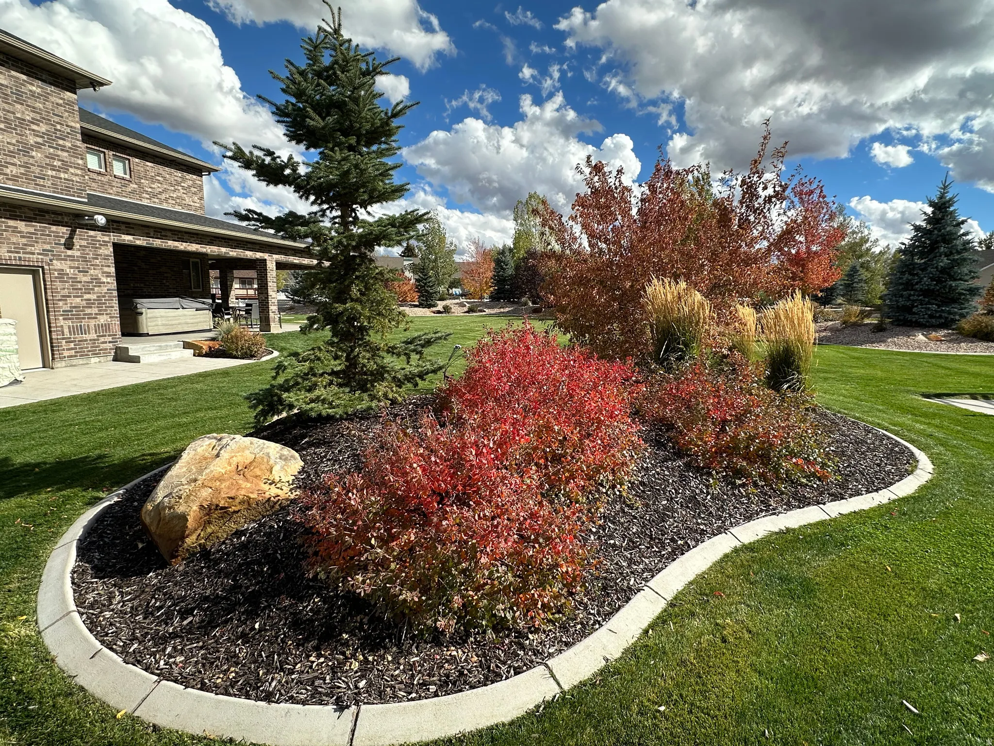 Curved landscape beds with colorful plantings, integrated boulder, and concrete curbing