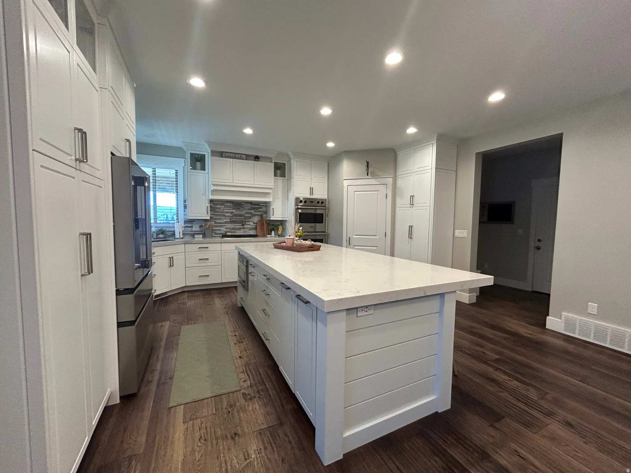 Gourmet kitchen featuring a large central island with a solid surface countertop, wood-finish flooring, recessed lighting, white shaker cabinetry, and stainless steel appliances