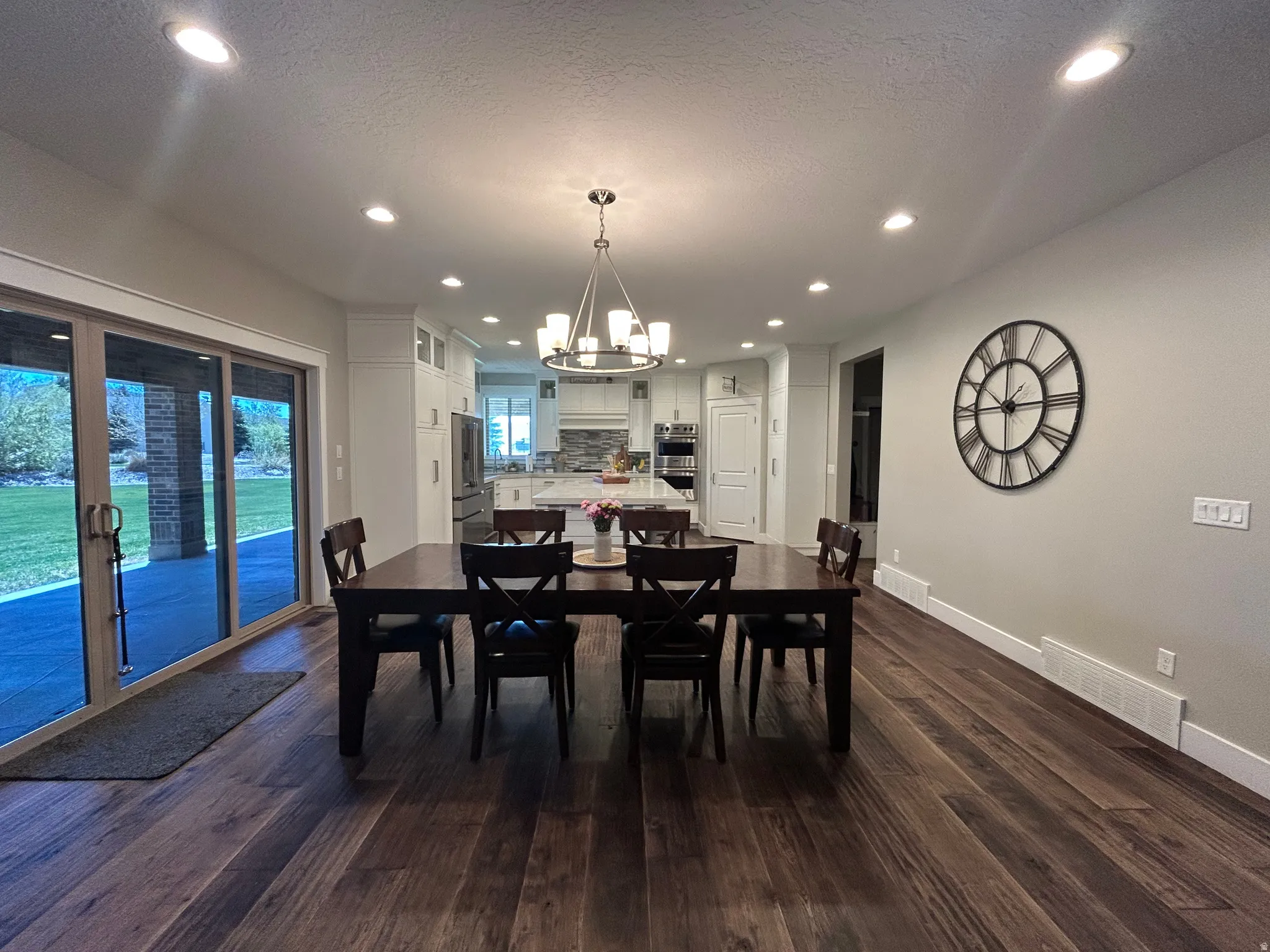 Spacious dining area featuring dark wood-finish flooring, recessed lighting, and a contemporary chandelier