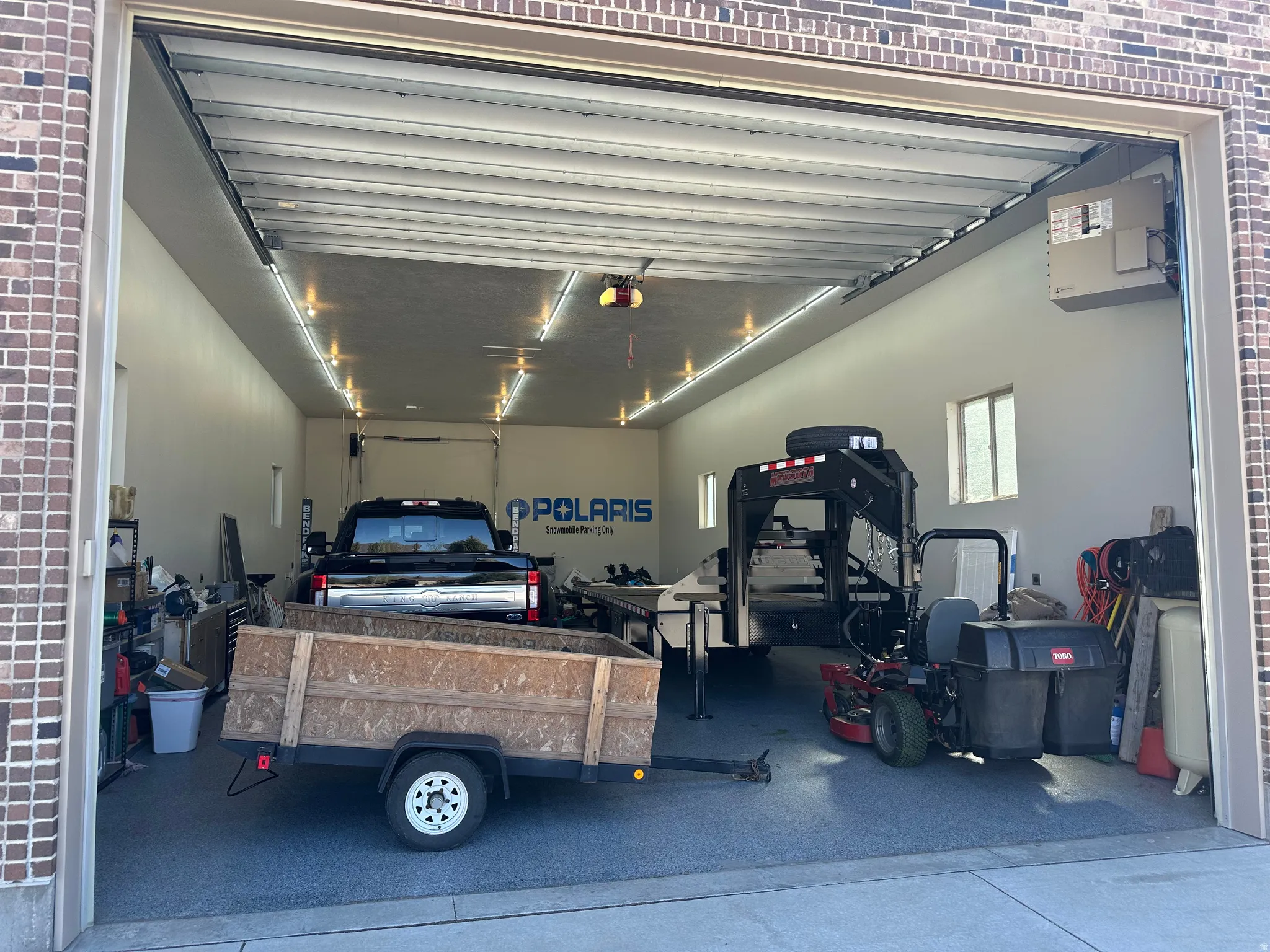 Spacious garage featuring a brick exterior, multiple strip lighting fixtures, a large overhead door, and two side windows