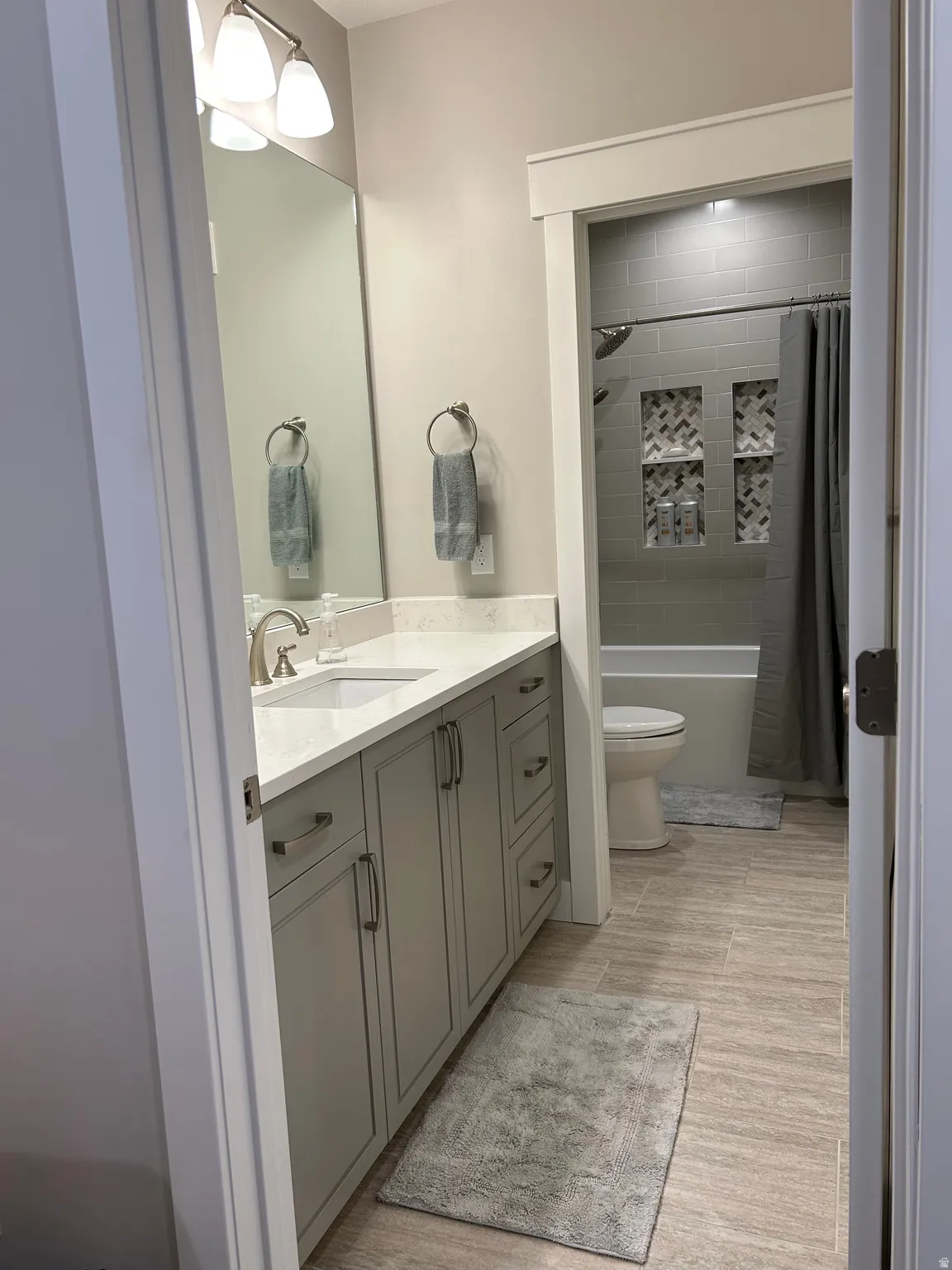 Contemporary bathroom featuring a light gray vanity with brushed nickel hardware, a white countertop, and an undermount sink