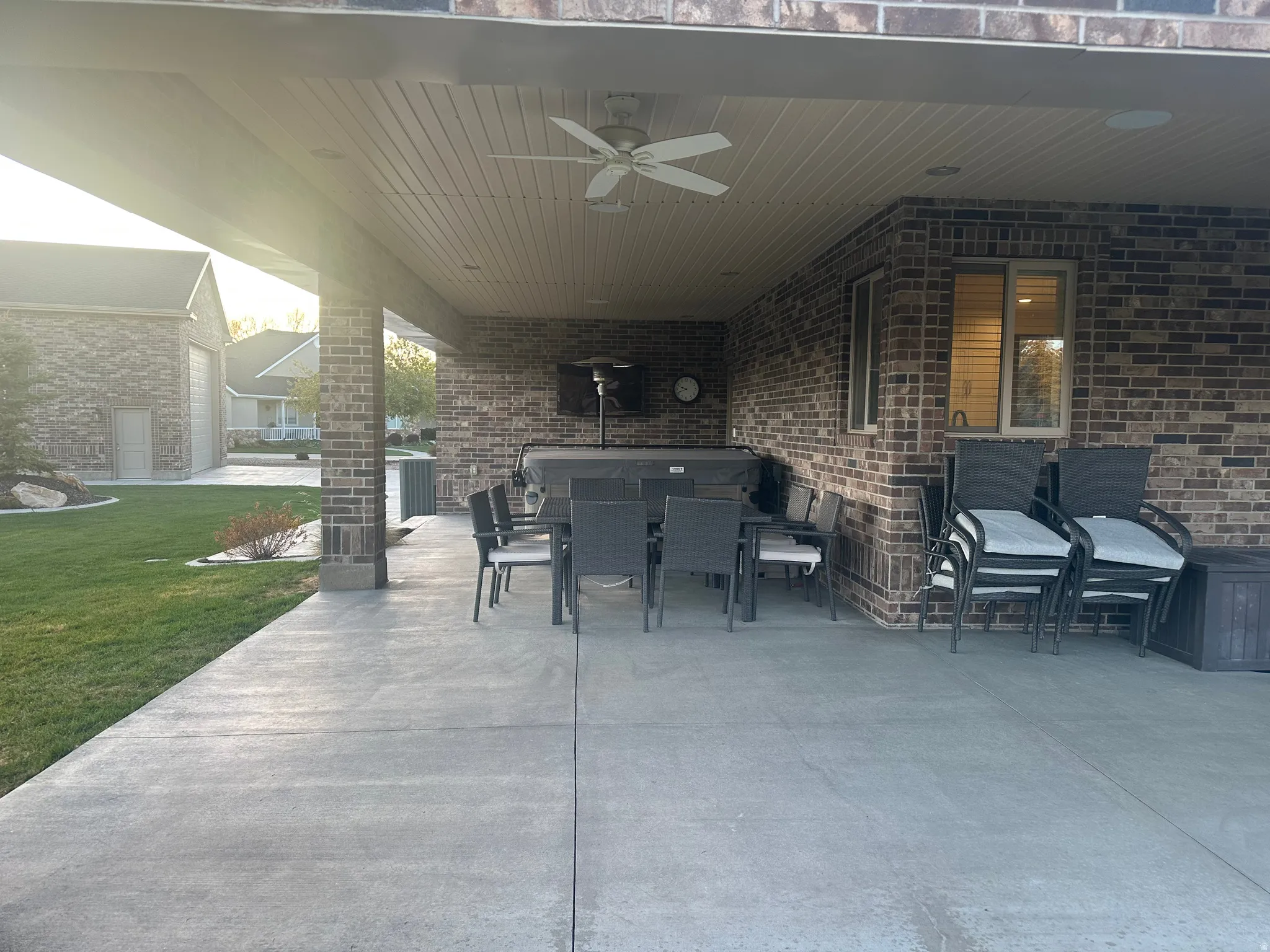 Expansive covered patio featuring a ceiling fan, brick exterior, concrete flooring, and a manicured lawn