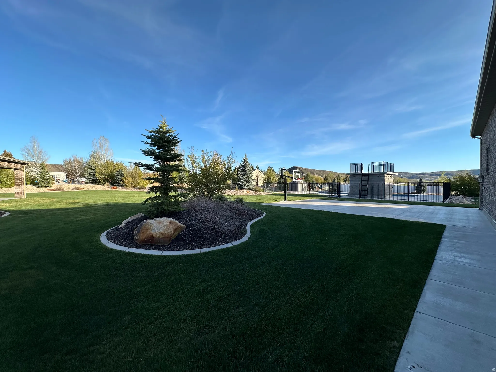 Expansive green lawn featuring a landscaped island with mature evergreen trees and natural rock elements