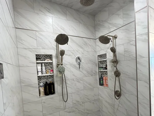 Expansive walk-in shower featuring white marble-look wall tiling and a gray tiled floor