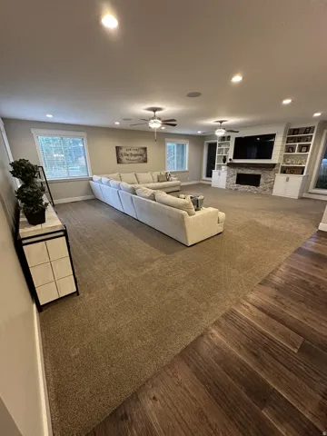 Spacious living area featuring recessed lighting, ceiling fans, and a stone-clad fireplace with built-in shelving