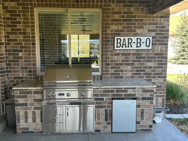 Outdoor kitchen featuring a built-in stainless steel grill, integrated storage drawers, and a compact refrigerator
