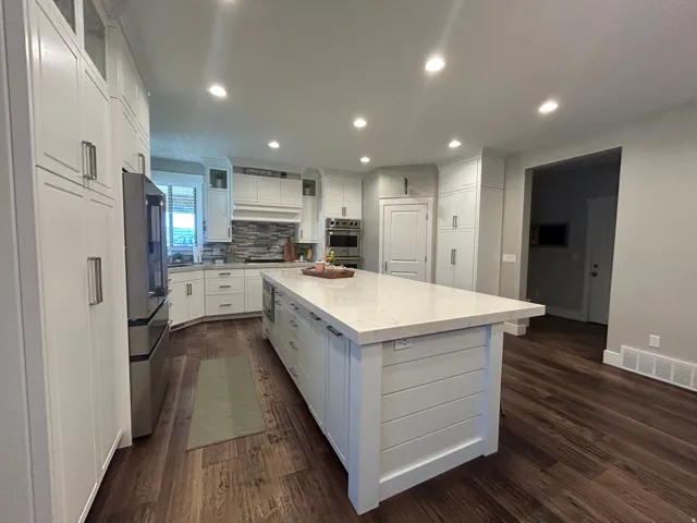 Gourmet kitchen featuring a large central island with a solid surface countertop, wood-finish flooring, recessed lighting, white shaker cabinetry, and stainless steel appliances