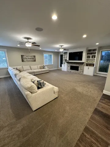 Spacious room featuring broadloom carpet, built-in shelving, a stone fireplace, wood-finish flooring, and recessed lighting