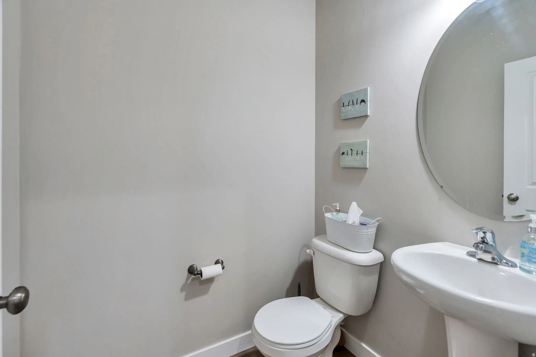 Powder room featuring a pedestal sink, round wall-mounted mirror, and white toilet