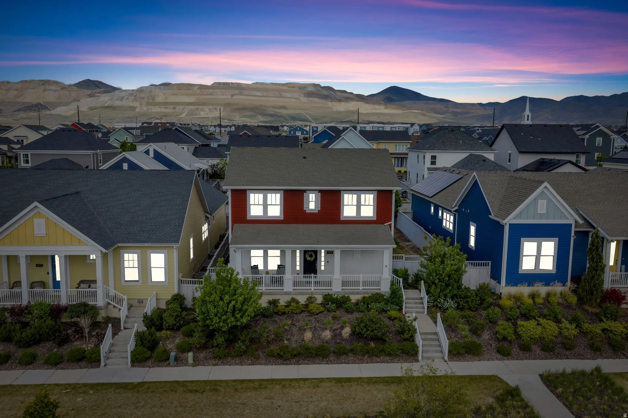 Red two-story residence featuring white window trim, a covered front porch, and an elevated landscaping design