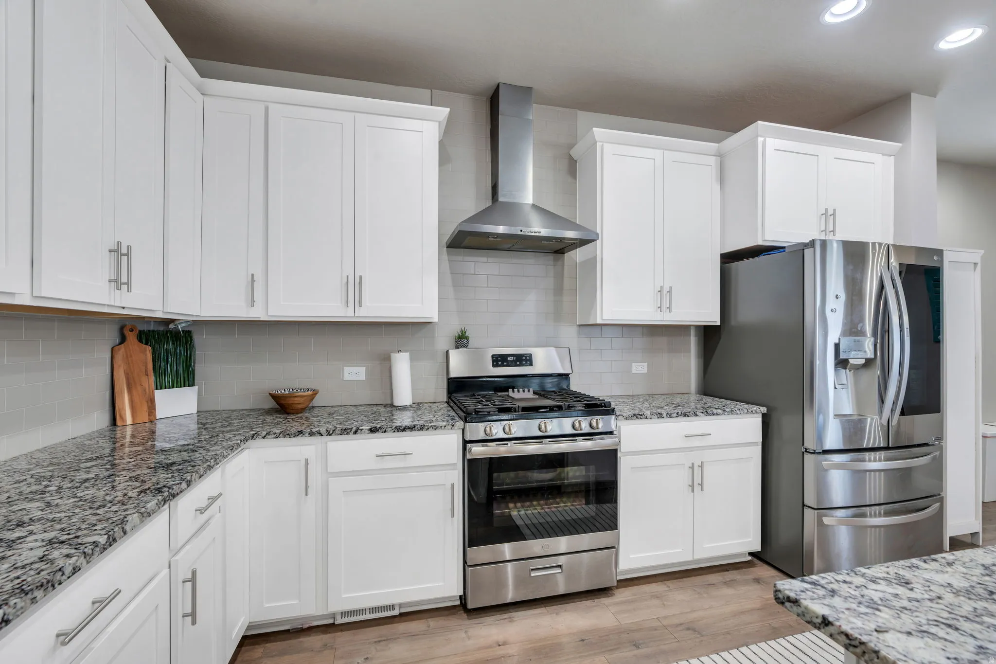 Kitchen featuring white shaker-style cabinetry, granite countertops, stainless steel appliances, a subway tile backsplash, and wood-finish flooring