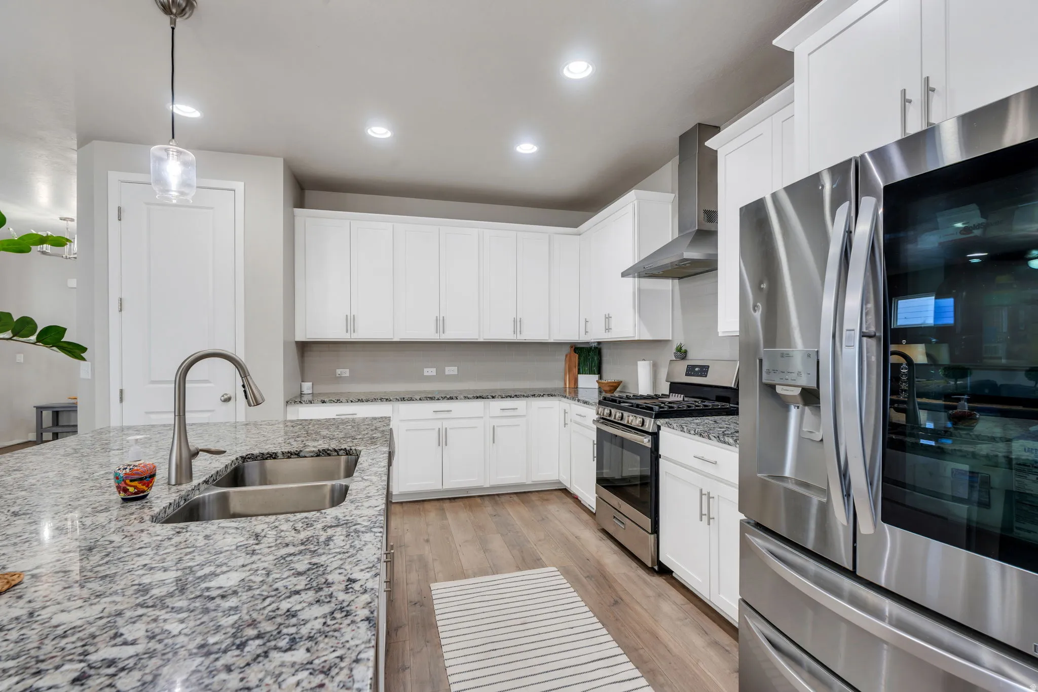 Modern kitchen featuring an island with a stainless steel double sink, a brushed nickel gooseneck faucet, and light-toned granite countertops