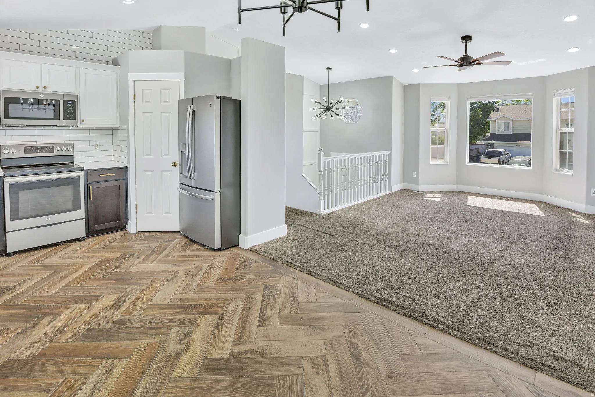 Kitchen with wood-finish flooring in a herringbone pattern, stainless steel appliances, white cabinetry, and subway tile backsplash