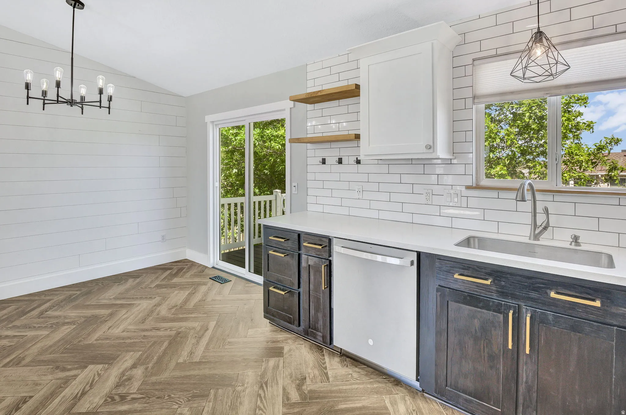Open-concept kitchen and dining area featuring herringbone wood-finish flooring, white shiplap accent wall, and a contemporary chandelier