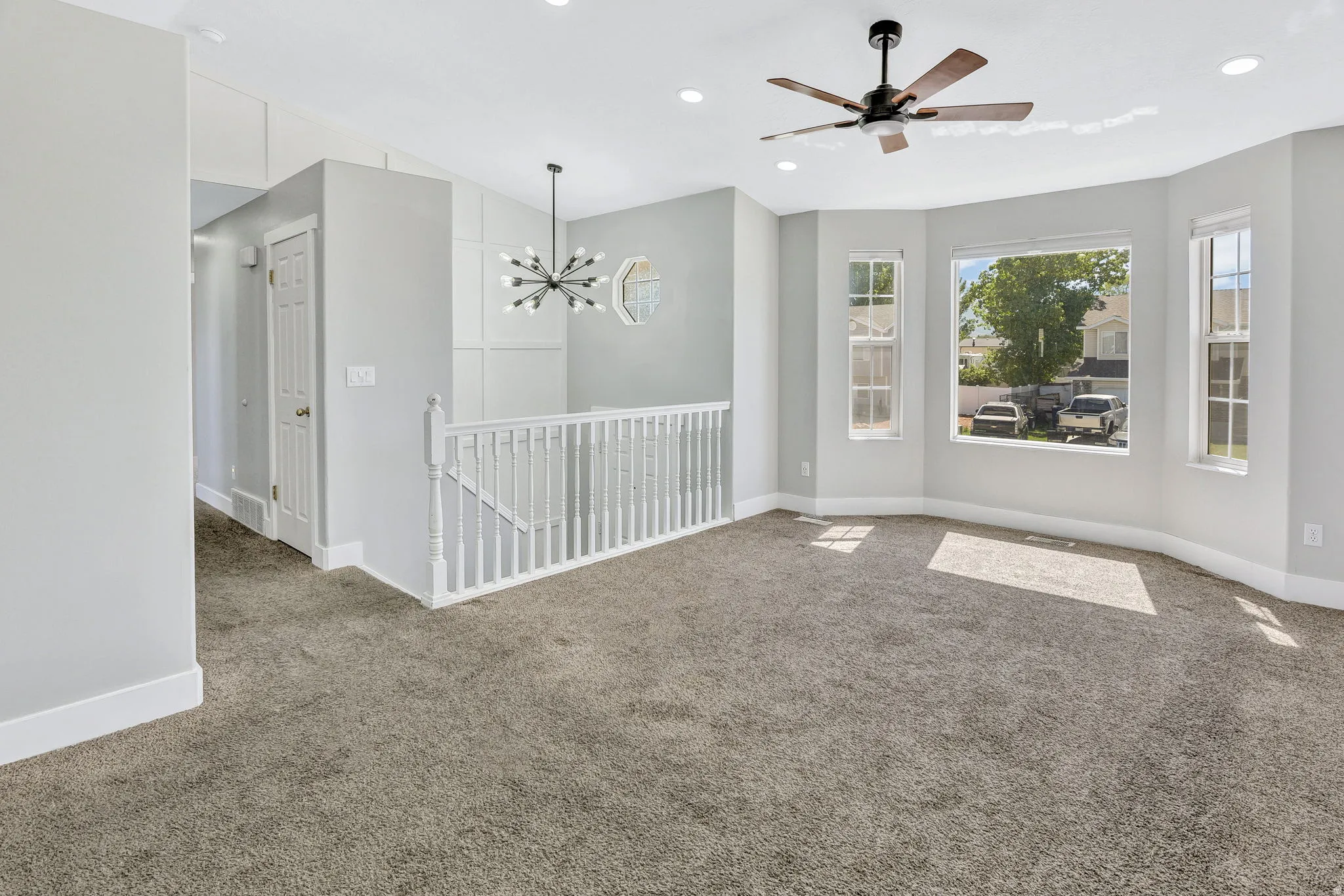 Spacious room featuring a tiered bay window, contemporary ceiling fan, recessed lighting, and soft grey carpeting