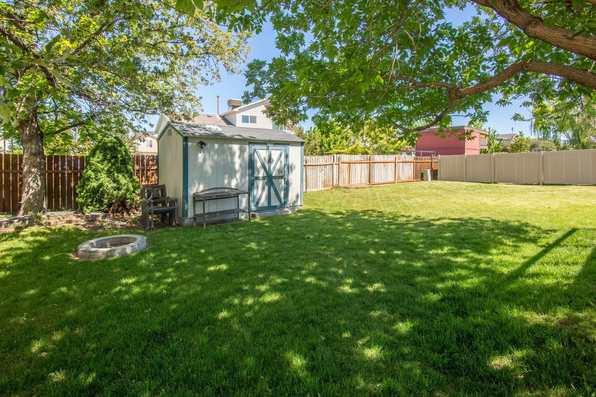 Spacious lawn featuring a storage shed, stone fire pit, wood fence, and mature trees