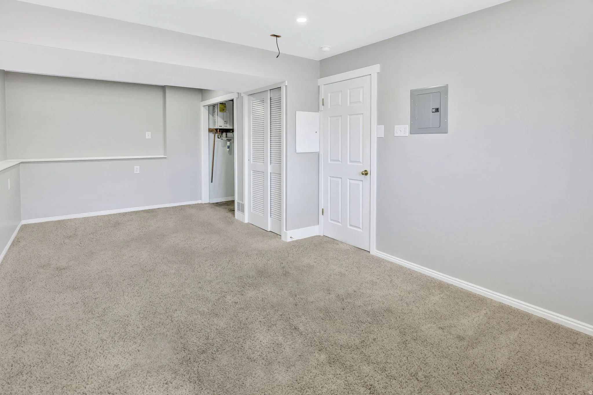Spacious room with light gray walls, plush carpeting, white trim, and recessed lighting