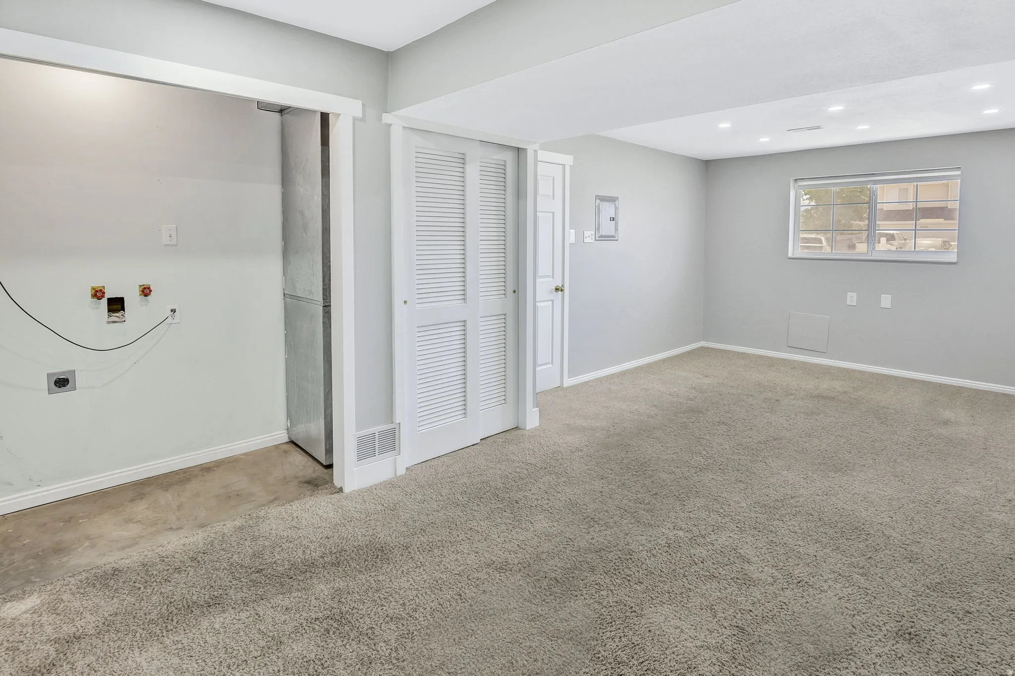 Carpeted interior space with a window, recessed lighting, white louvered bifold doors, and a laundry hookup area with a concrete floor