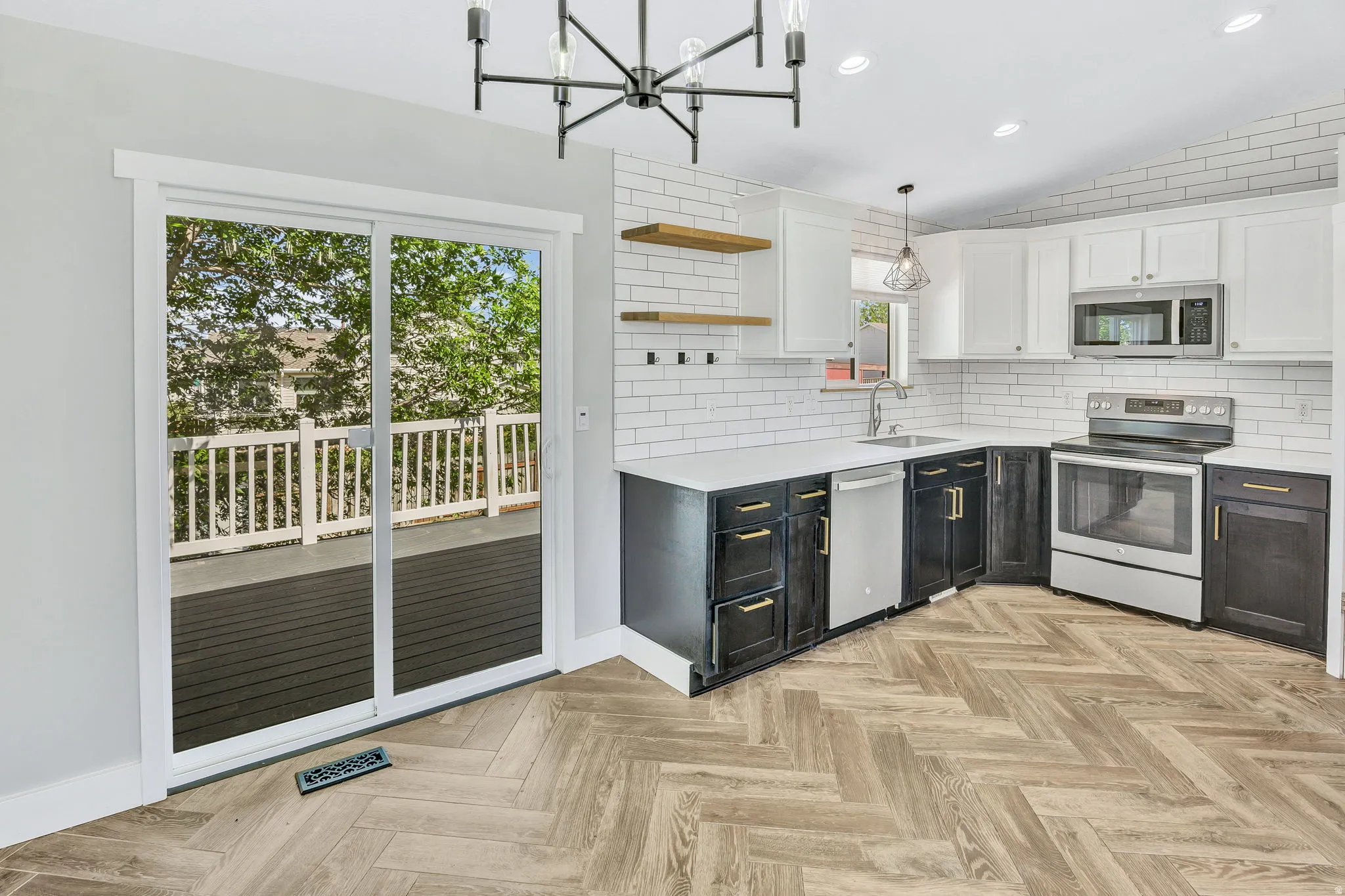 Kitchen featuring black and white cabinetry, a white subway tile backsplash, stainless steel appliances, and wood-finish herringbone flooring