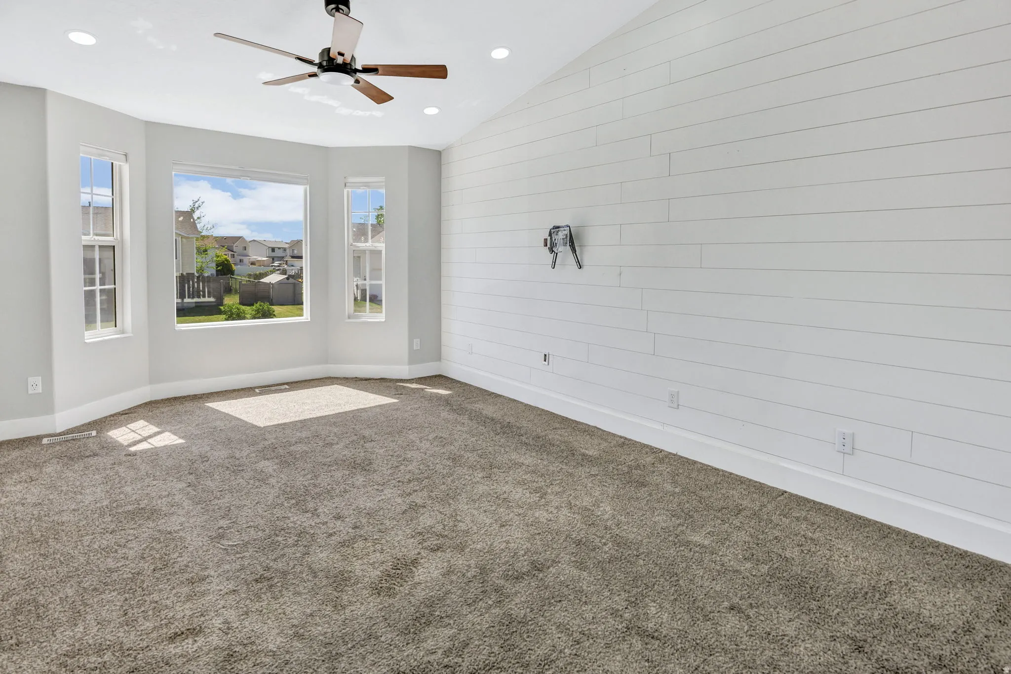 Room featuring a bay window, shiplap accent wall, vaulted ceiling, recessed lighting, and a ceiling fan with wood-finish blades