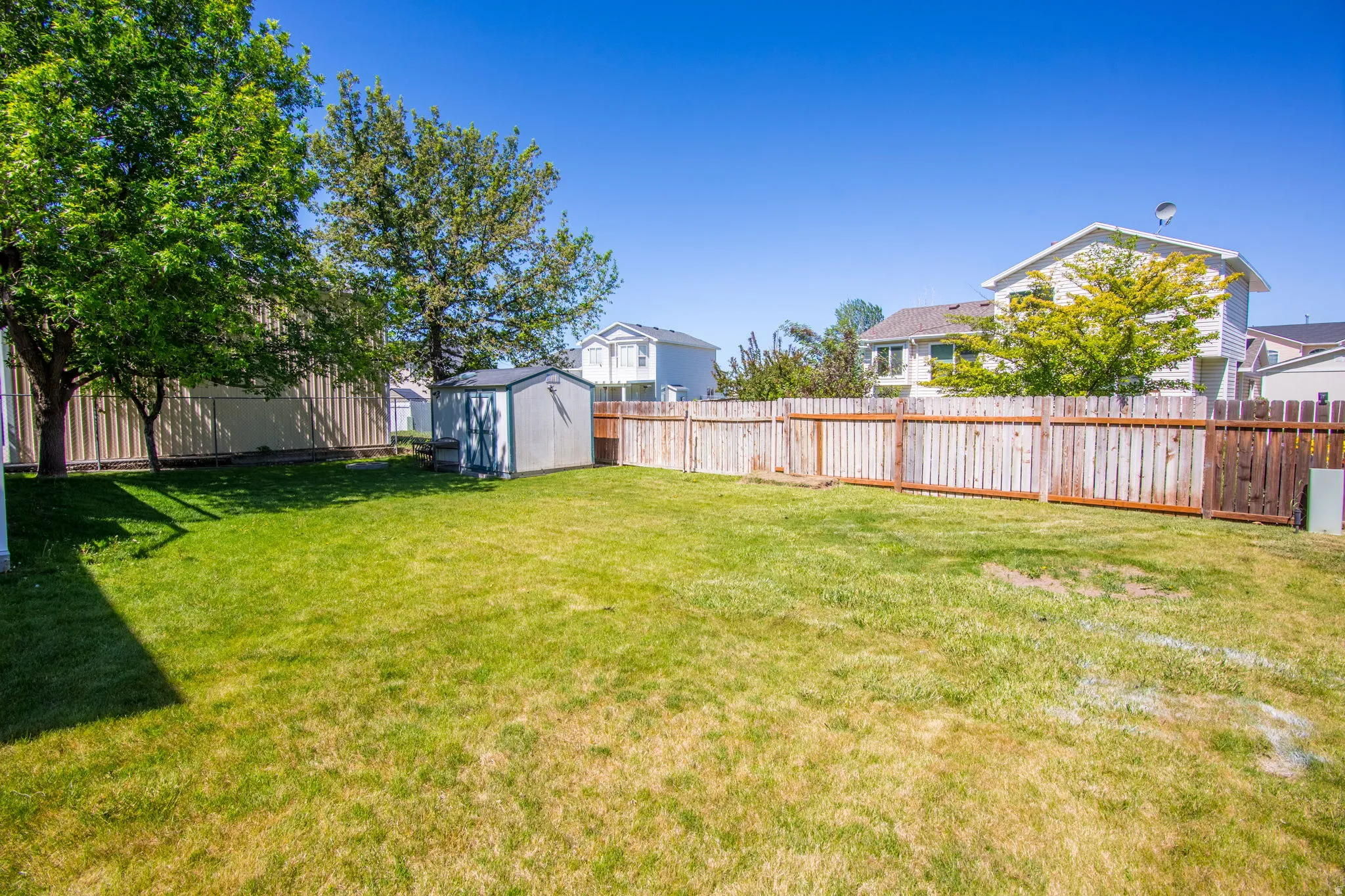 Expansive grass lawn featuring a metal storage shed and mature trees