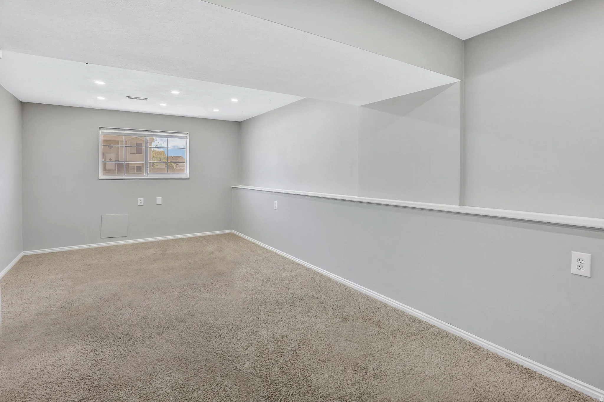 Spacious carpeted room featuring recessed lighting, a window, and light gray walls with white trim