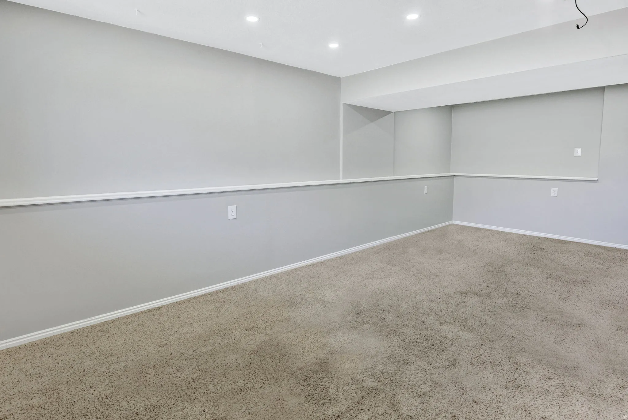Spacious room featuring neutral carpeting, light gray wall paint, white trim, recessed lighting, and a drop ceiling with integrated lighting