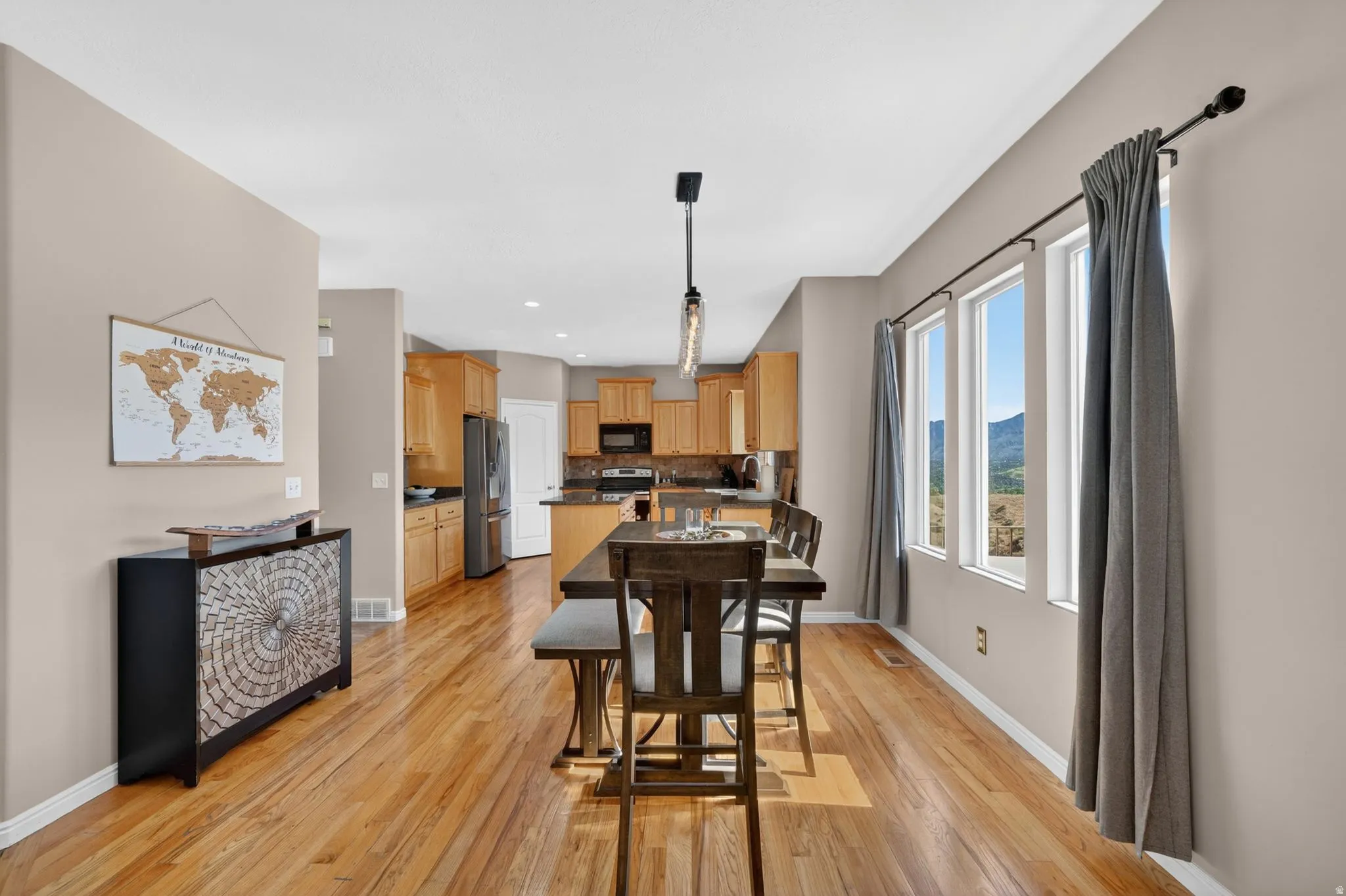 Dining area with natural wood-finish flooring, three large windows, and a multi-bulb linear pendant light