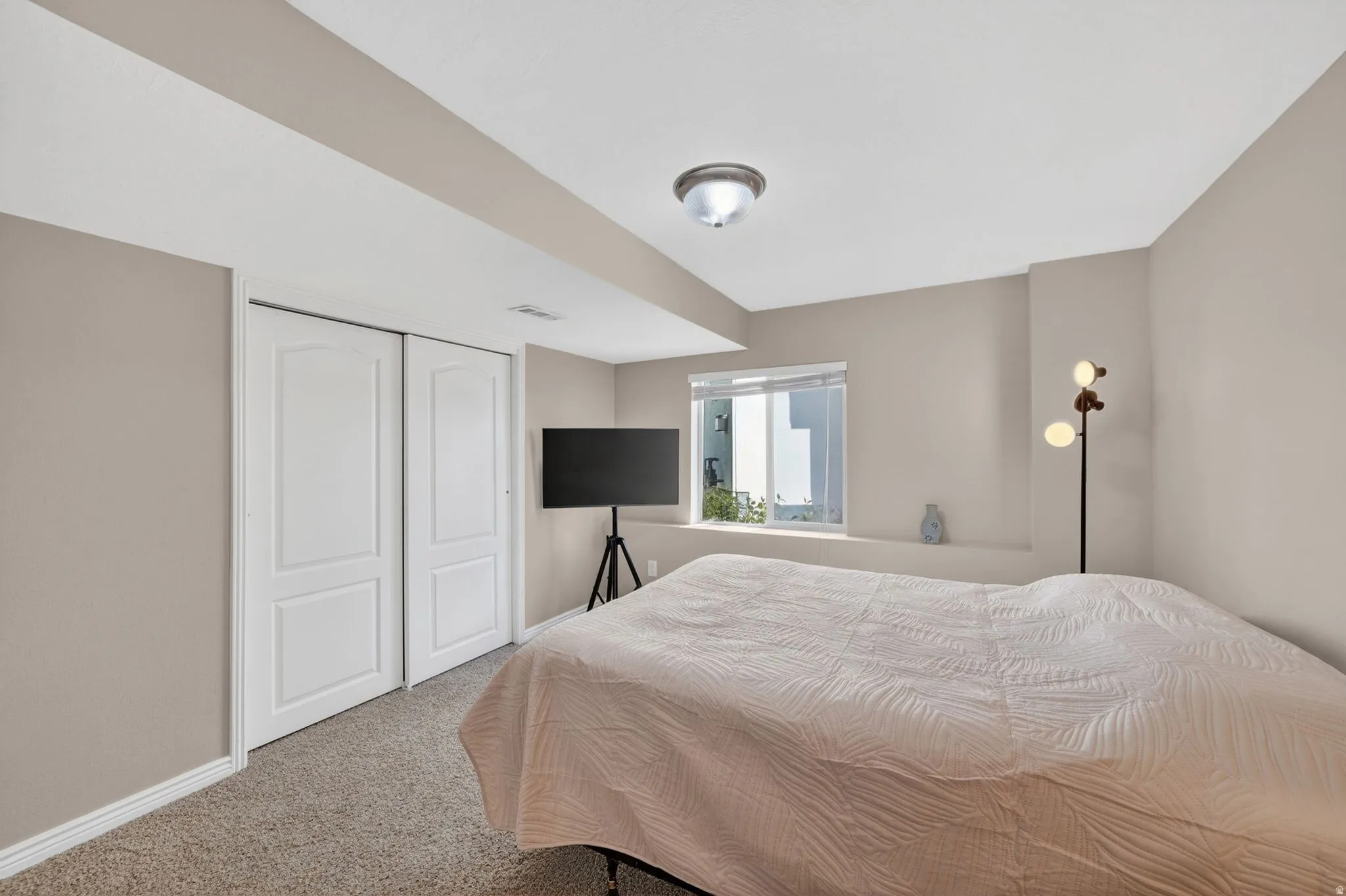 Carpeted room featuring a window with white blinds, neutral wall paint, white baseboards, and two white bi-fold closet doors