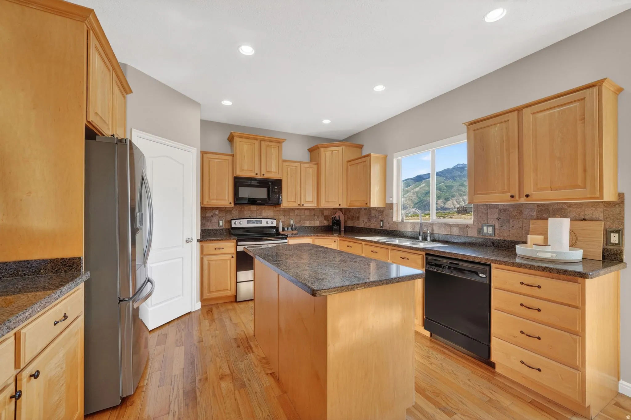 Open-concept kitchen featuring light wood cabinetry, granite countertops, wood-finish flooring, a central island, and a mountain backdrop
