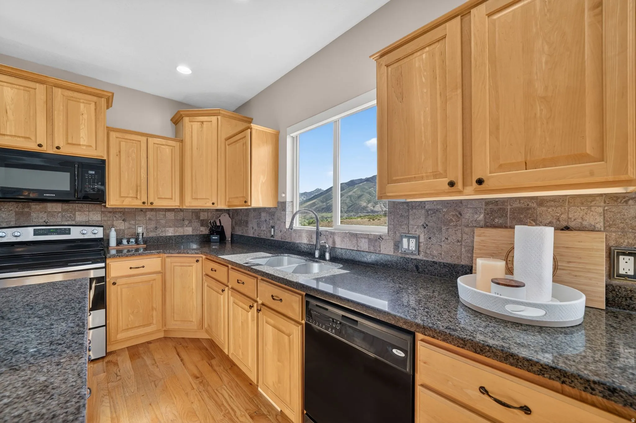 Kitchen featuring light wood cabinetry, dark speckled countertops, and a tiled backsplash