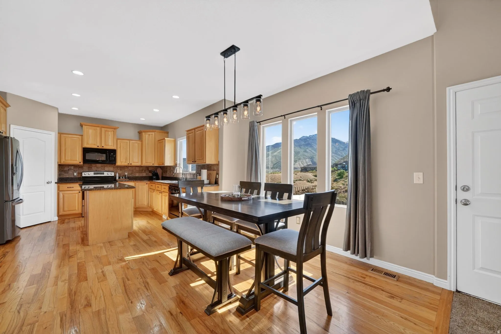 Kitchen and dining area featuring wood-finish flooring, light-toned cabinetry, a central island, stainless steel appliances, and a window wall overlooking mountains