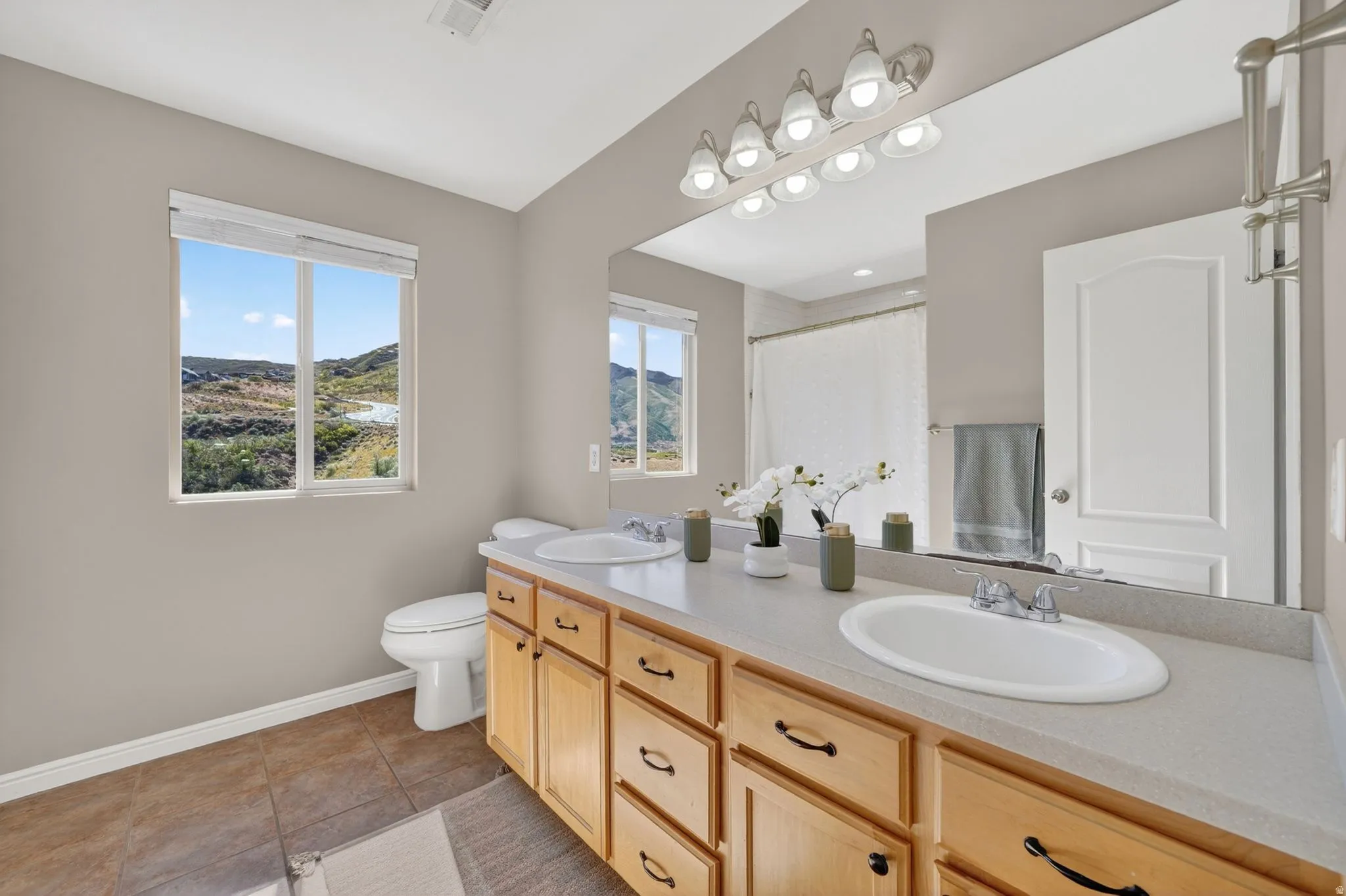 Bathroom featuring a dual vanity with light wood cabinetry, a large wall-mounted mirror, and tile flooring